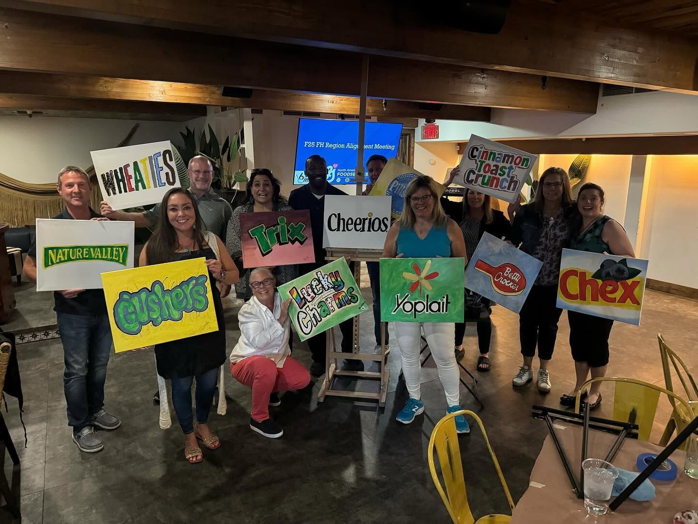 Group of people indoors holding colorful cereal-box signs and smiling for a photo.
