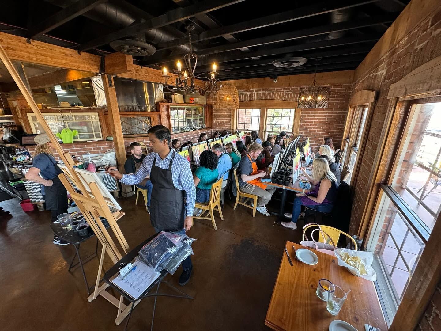 Busy rustic café with people seated at wooden tables under exposed beams and warm sunlight.