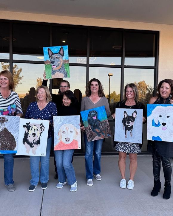 Group standing outside holding painted pet portraits in front of a building.