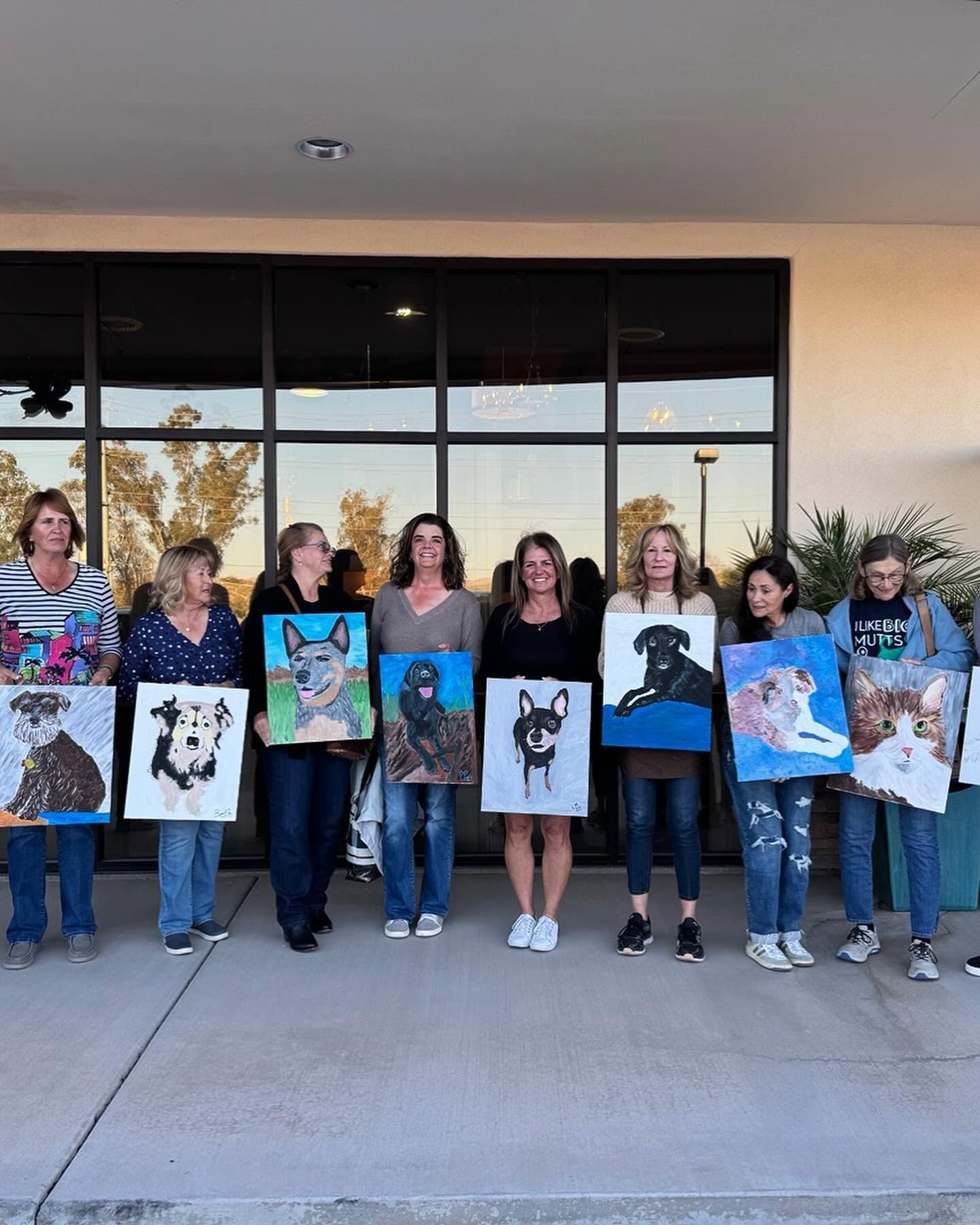 Group of people holding animal paintings outside a building with glass doors.