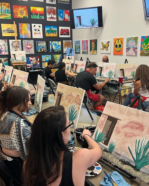 People painting colorful landscapes in an art class, with completed paintings displayed on the wall.