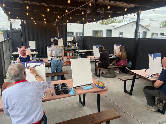 People painting at easels under string lights in an outdoor patio art class