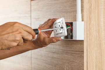 Hands using a screwdriver to install an electrical outlet on a wooden wall