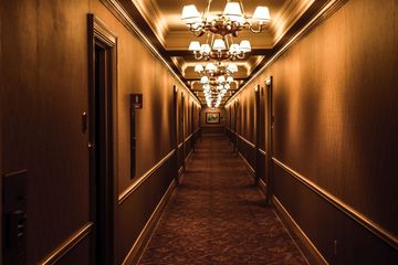 Dimly lit hotel hallway with chandeliers, carpet, and wood-paneled walls
