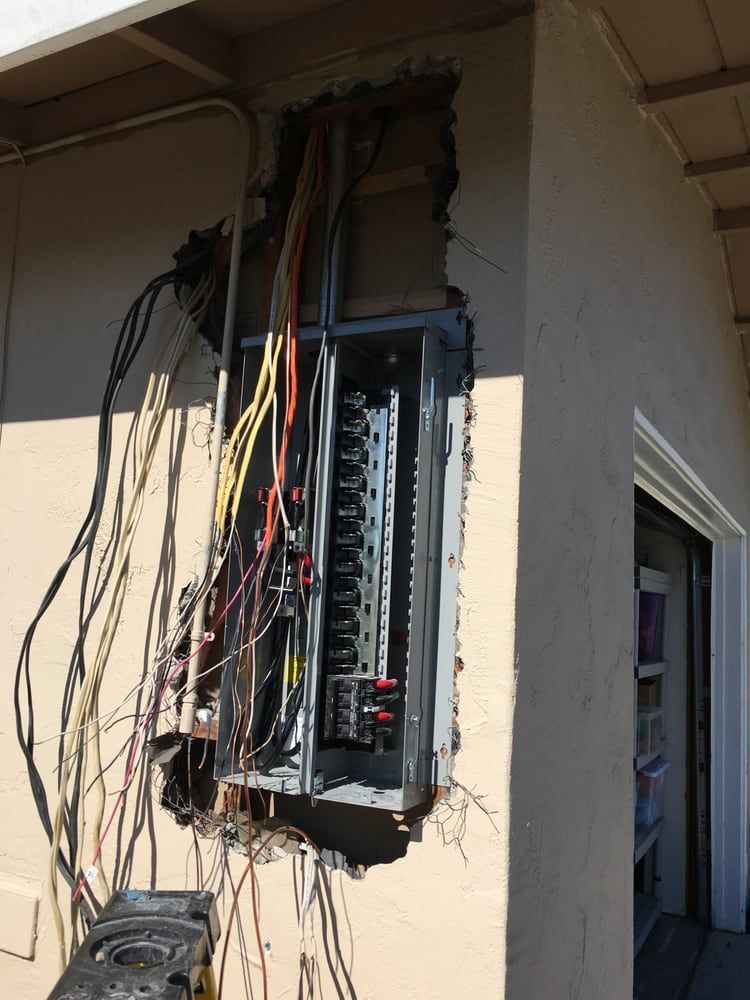 Open electrical panel with exposed wiring mounted on an exterior wall near a doorway