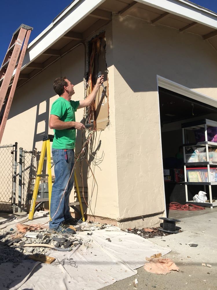 Worker in green shirt repairing wiring on the exterior of a building under construction.