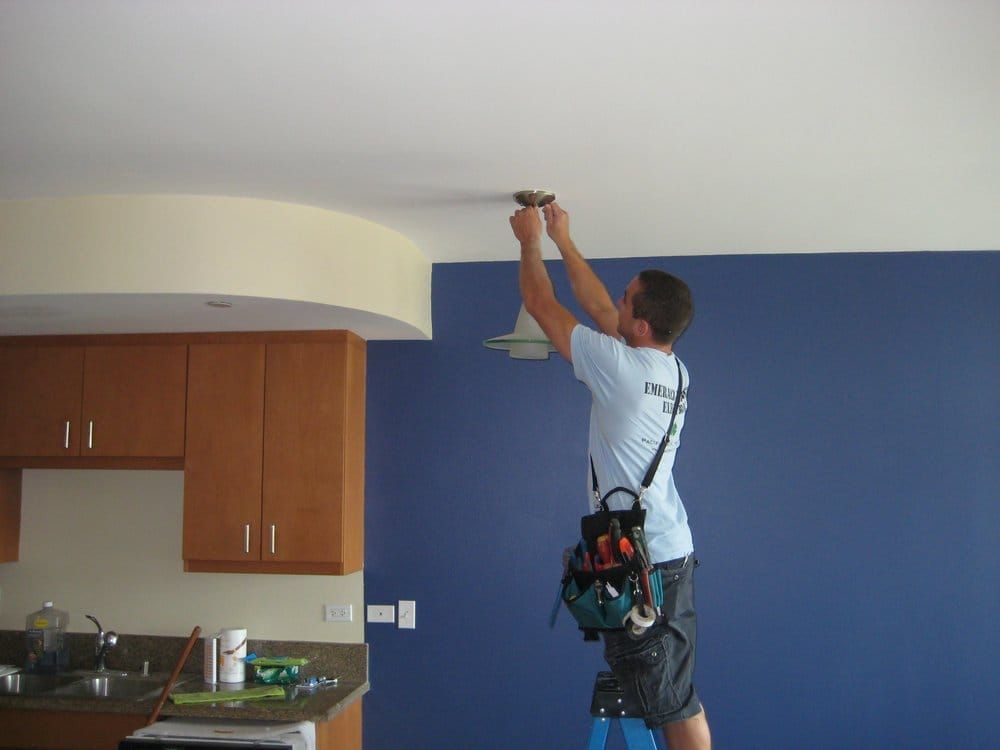 Worker installing a ceiling fixture in a room with blue walls and kitchen cabinets