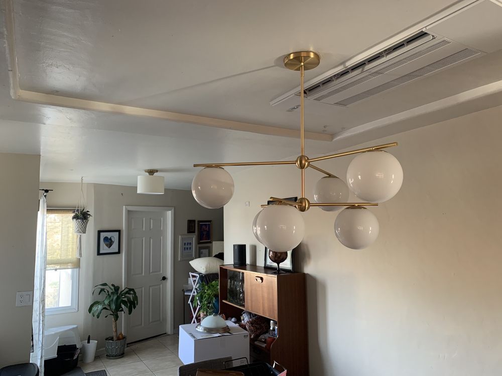 Living room with brass chandelier, white globe lights, and a wooden cabinet against a cream wall