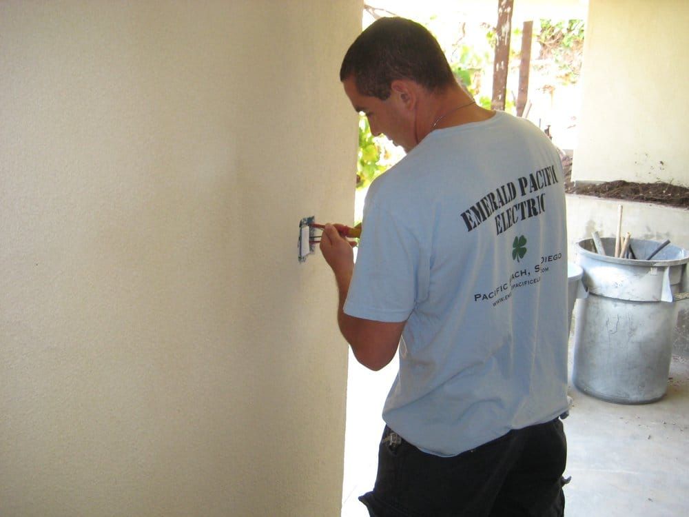 Person painting a wall with a small brush in a bright outdoor area