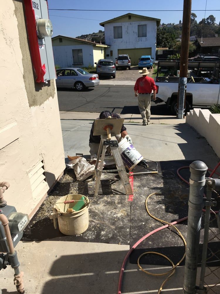 Worker in red shirt on a front walkway with construction tools and debris beside a house.