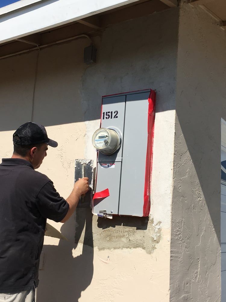 Person installing a red-and-white electric meter box on an exterior wall