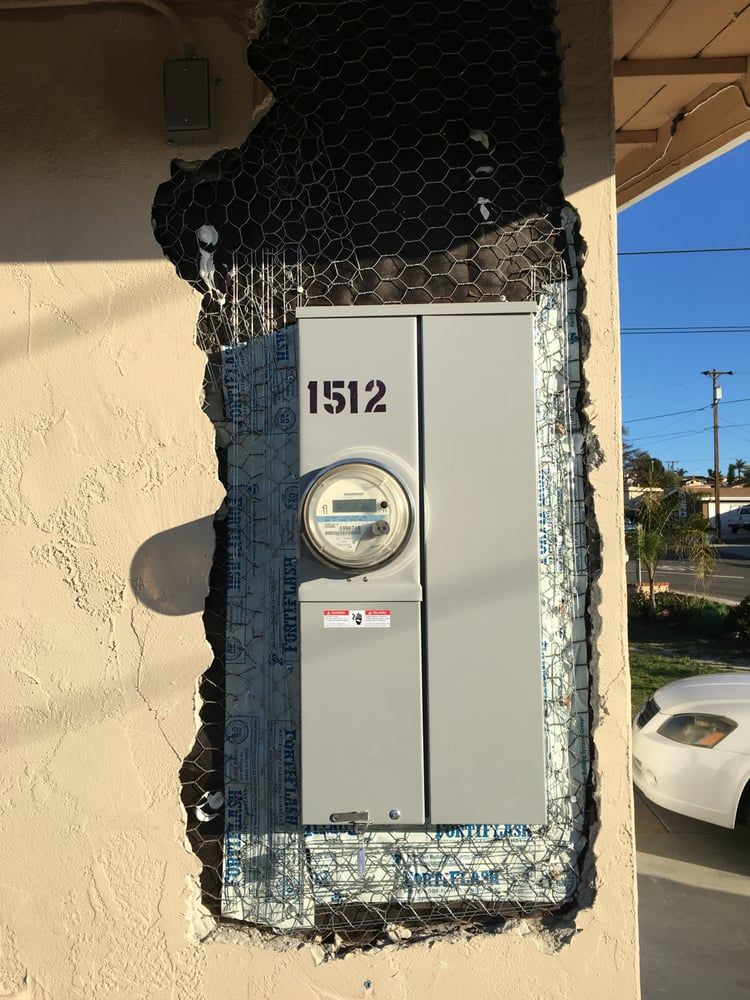 Residential electric meter panel mounted on a stucco wall with blue sky and a parked car nearby