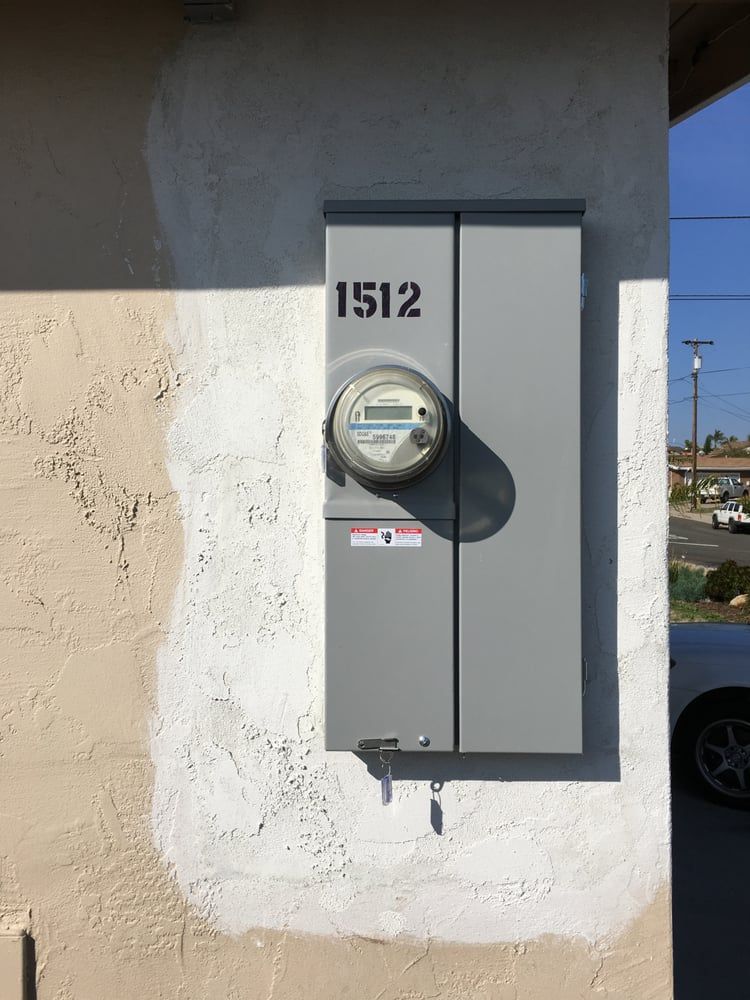 Gray utility meter box on a stucco wall with house number 1512 and a round electric meter.