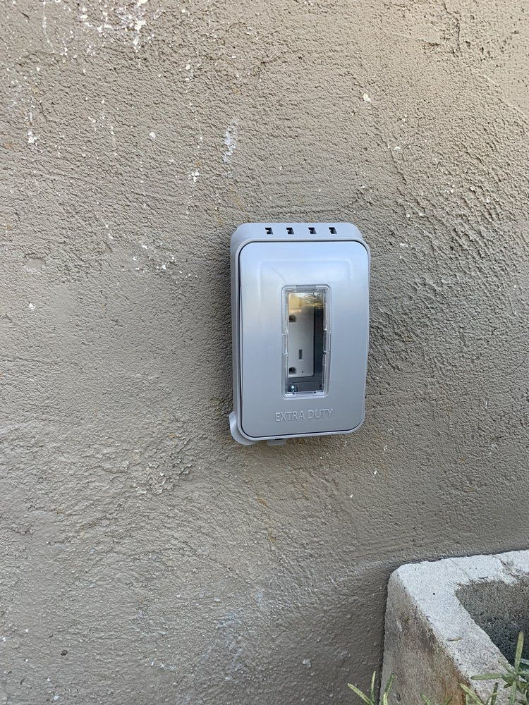 Gray electrical switch plate mounted on a beige stucco wall near a concrete edge.