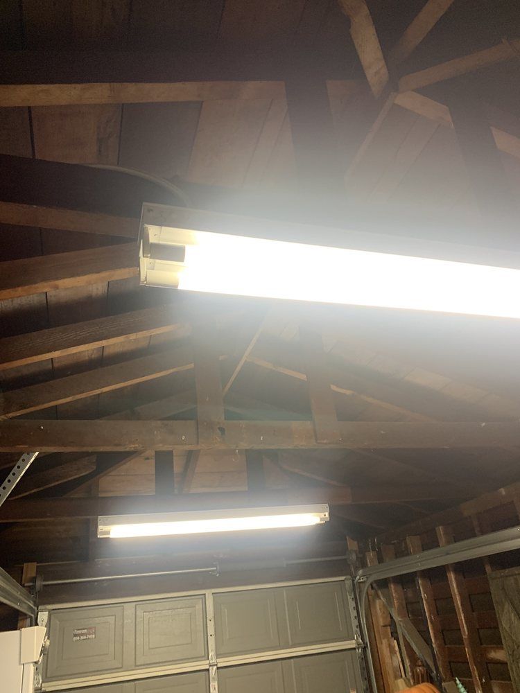 Dim garage interior with exposed wooden rafters and two bright fluorescent lights.