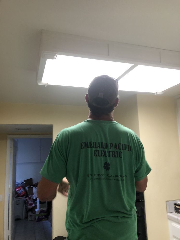 Person in a green T-shirt standing under a ceiling light fixture in a room.