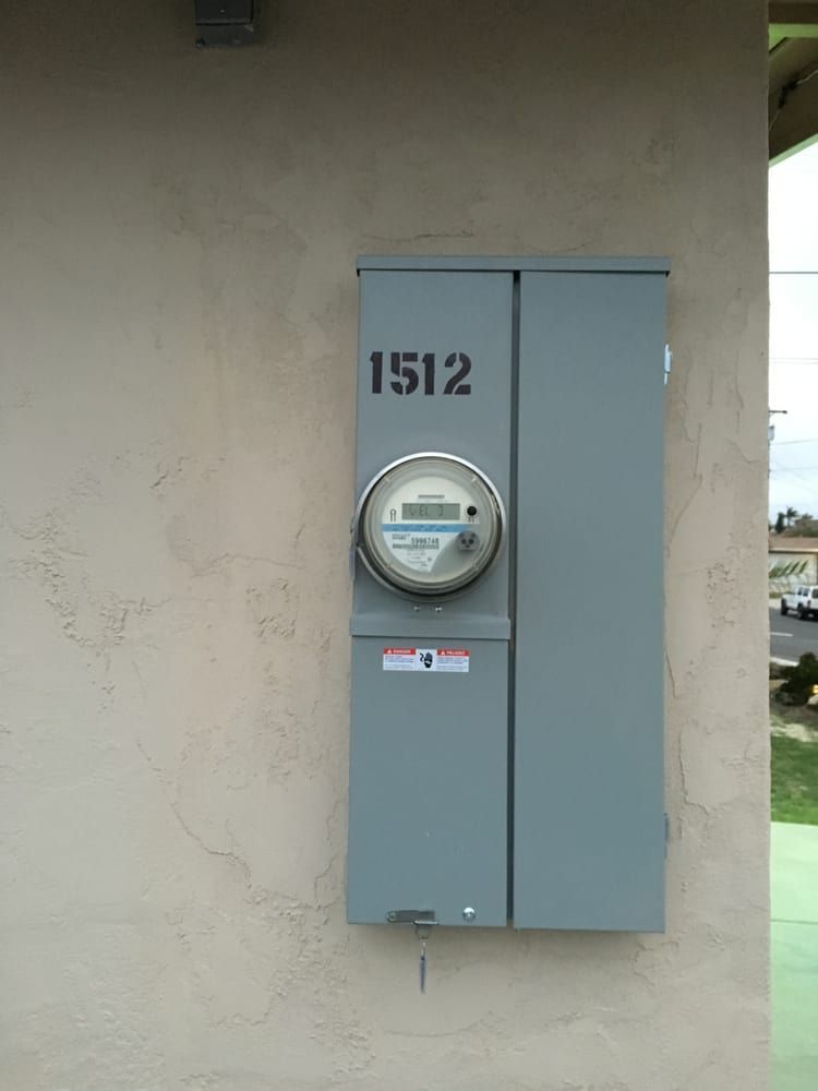 Gray electrical meter box labeled 1512 mounted on a beige exterior wall.
