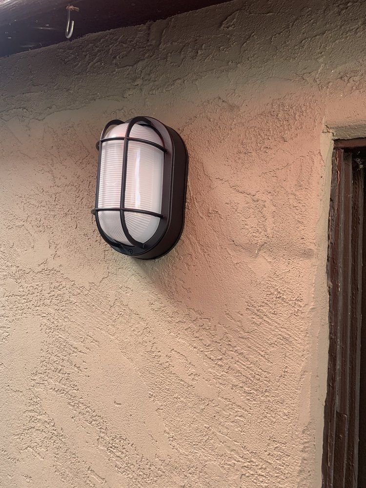 Black outdoor wall light on a beige stucco wall beneath an overhang