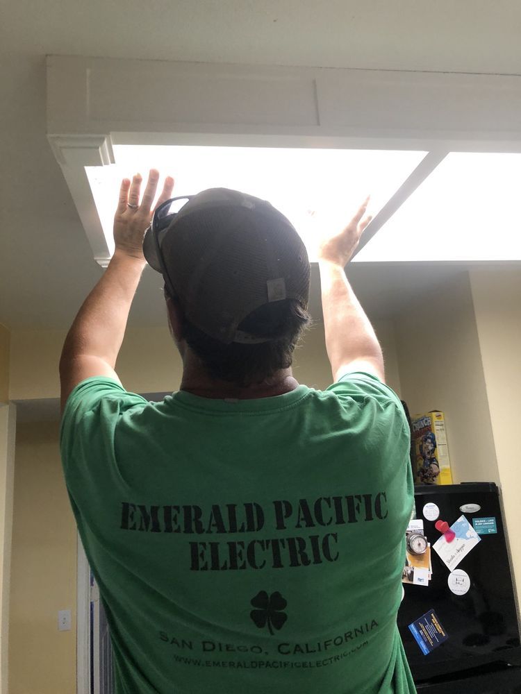 Worker in a green shirt adjusting a ceiling light panel in an indoor utility room