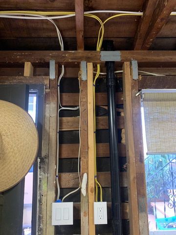 Unfinished wall with exposed wiring, ladder, and light switches in a garage or basement.