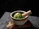 A stone mortar filled with green seaweed, topped with garlic and chili, sits on a wooden base against a black background.