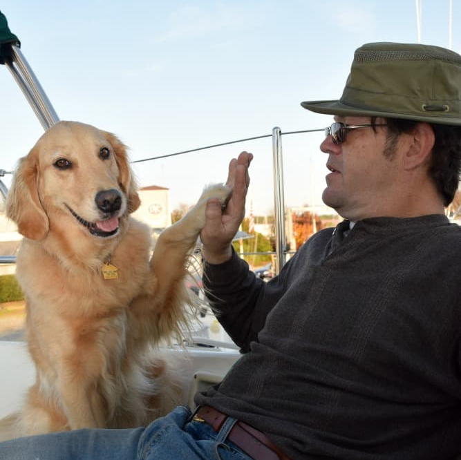 Golden retriever giving a high-five to a man on a boat. Dog is smiling. Man wearing a hat.