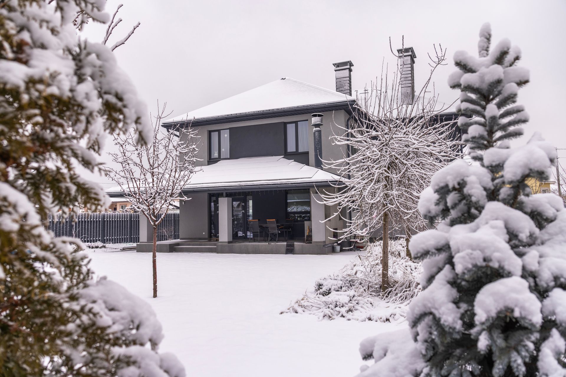 Snow-covered house and yard with trees in winter.
