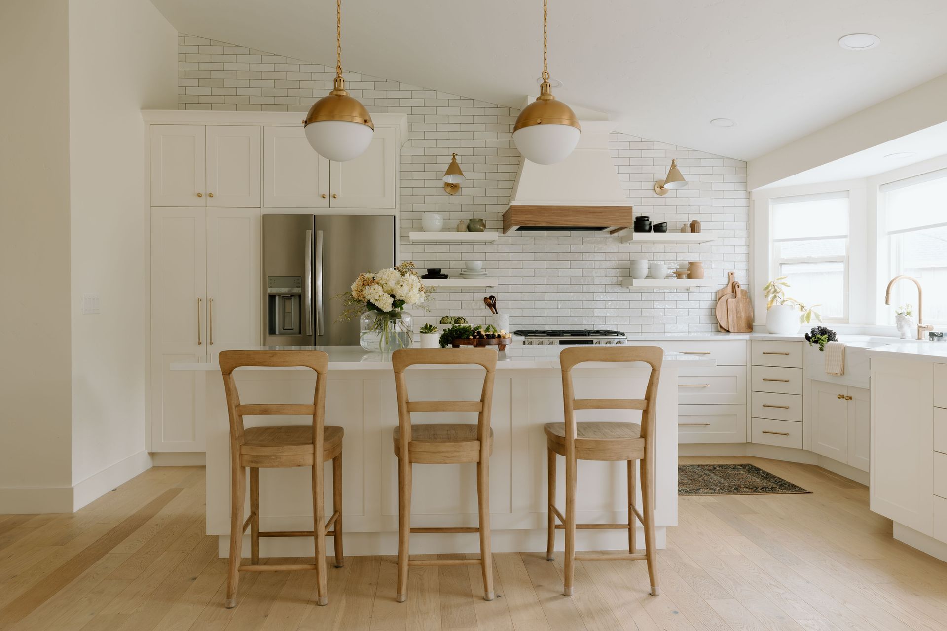 Bright white kitchen with island, wooden stools, pendant lights, and large windows