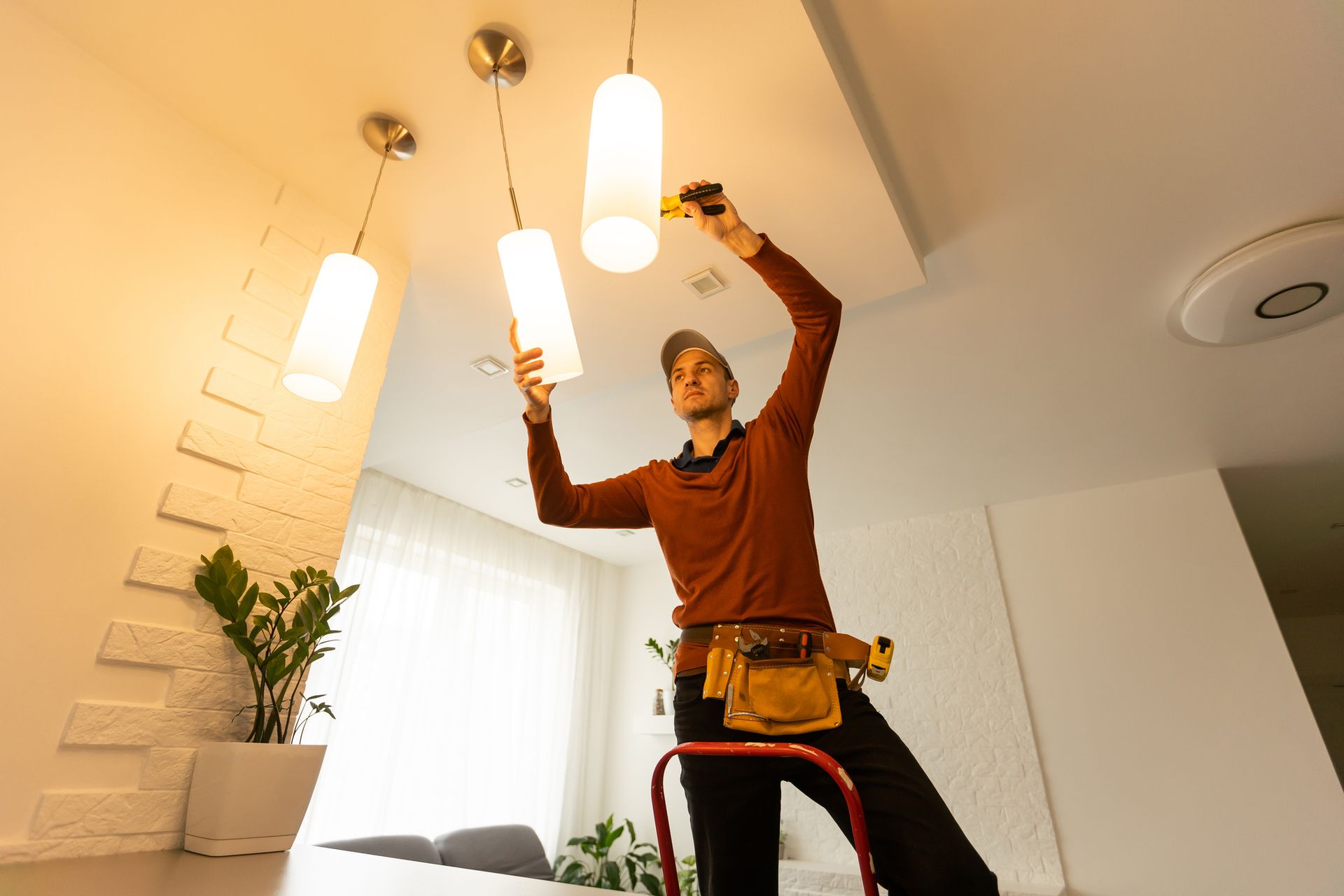 Person standing on a ladder installing ceiling light fixtures in a bright room