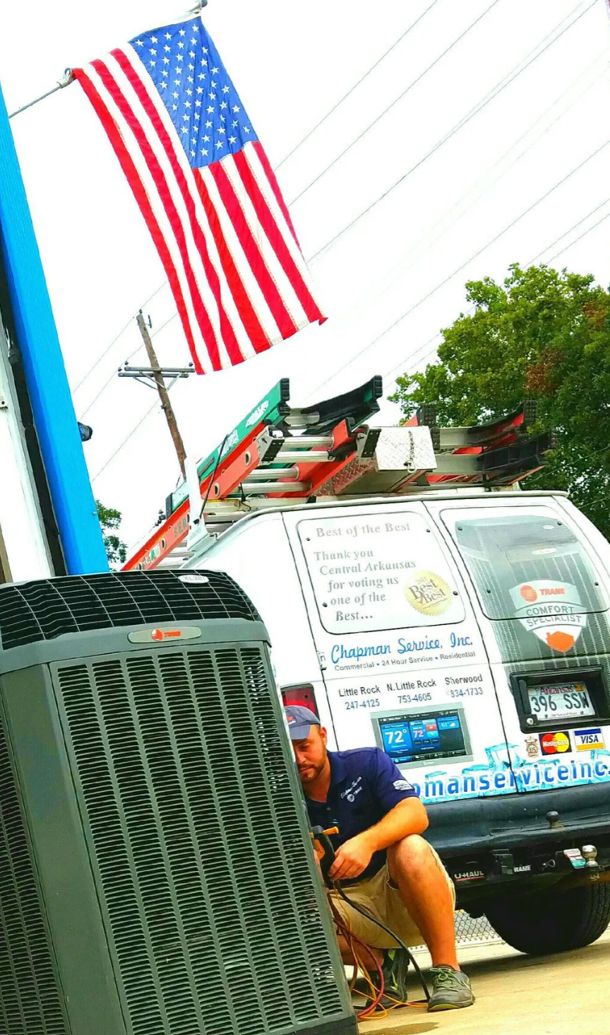 American flag waving above a parked van with a person sitting nearby on a city street.
