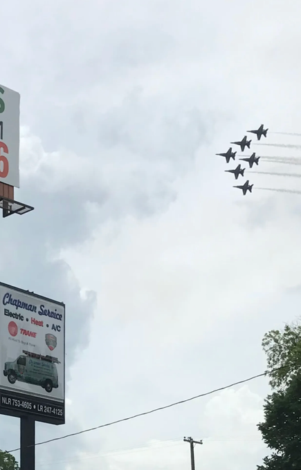 Six fighter jets flying in formation over city signs and a cloudy sky