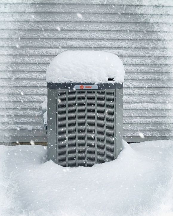 Snow-covered outdoor air conditioner against a corrugated wall