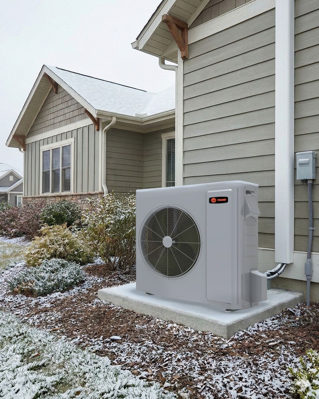 Outdoor heat pump unit beside a beige house in a snowy yard