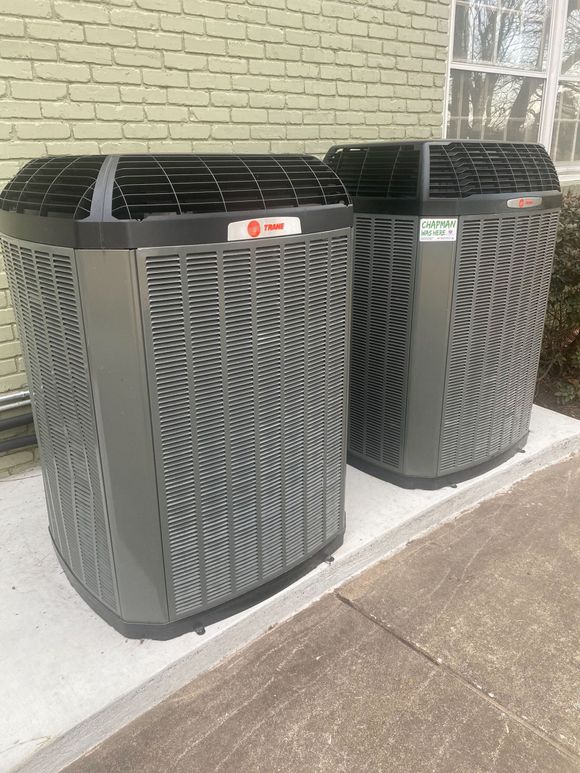 Two large gray HVAC units beside a brick wall on a sidewalk