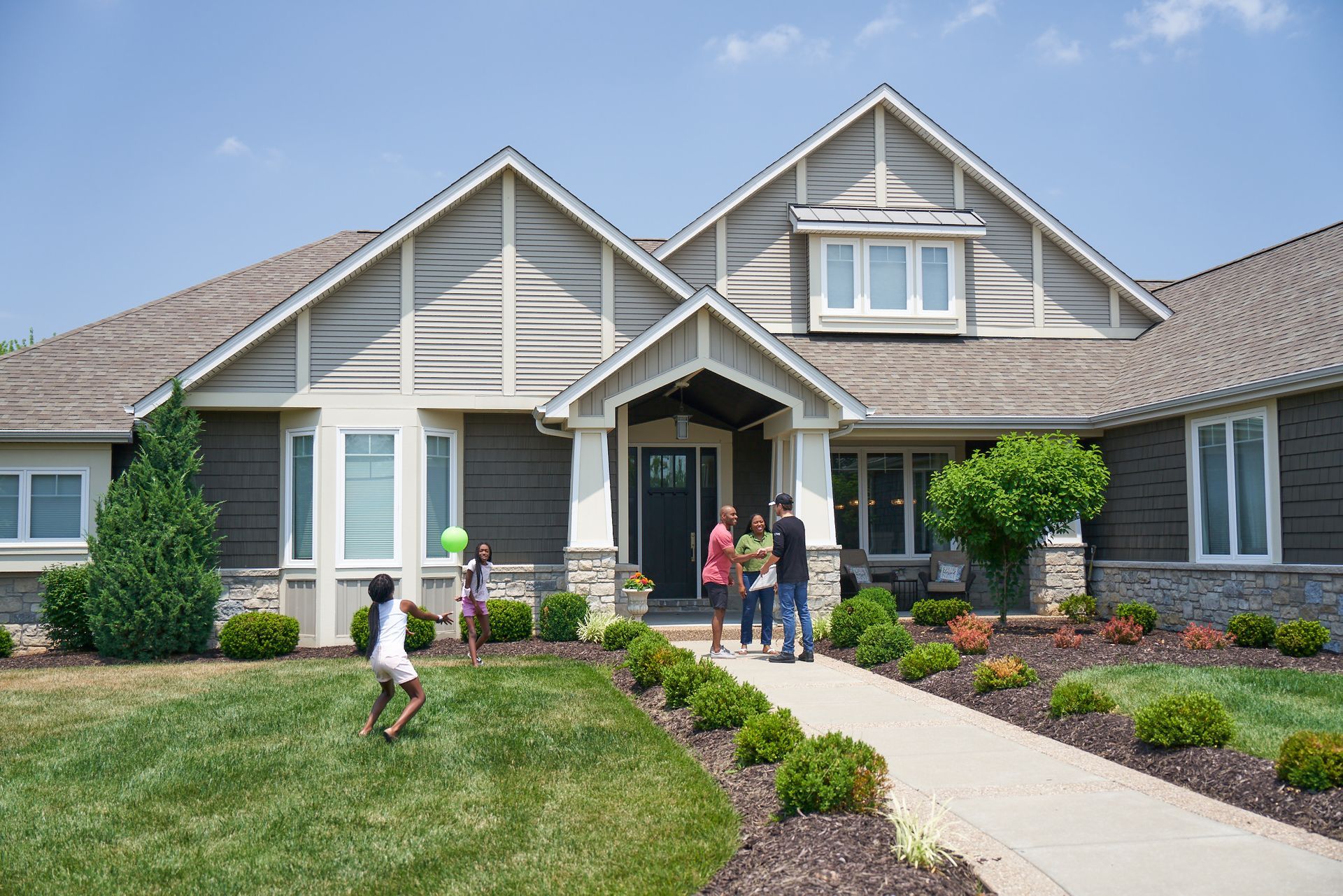 Family standing outside a gray suburban home with a manicured lawn and front walkway