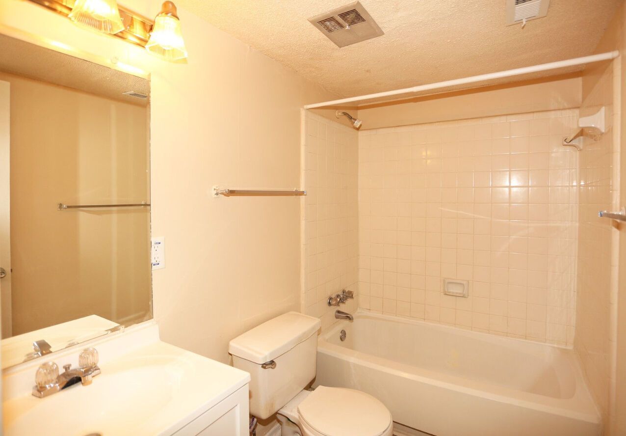 A bathroom with a toilet , sink , tub and mirror.