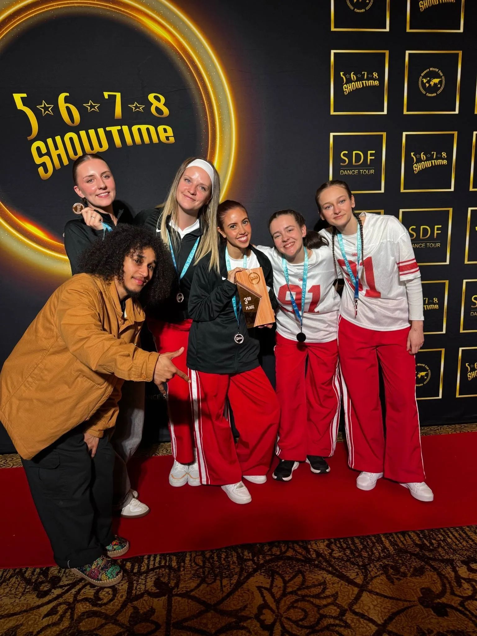 Six personnes posant sur un tapis rouge devant un fond de scène Shoutout, souriantes dans des tenues colorées