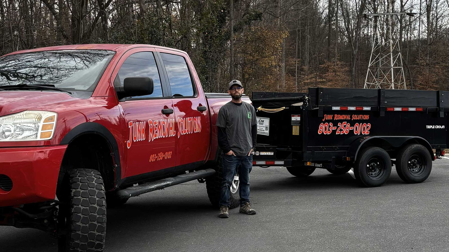 A man is standing next to a red truck with a trailer attached to it.