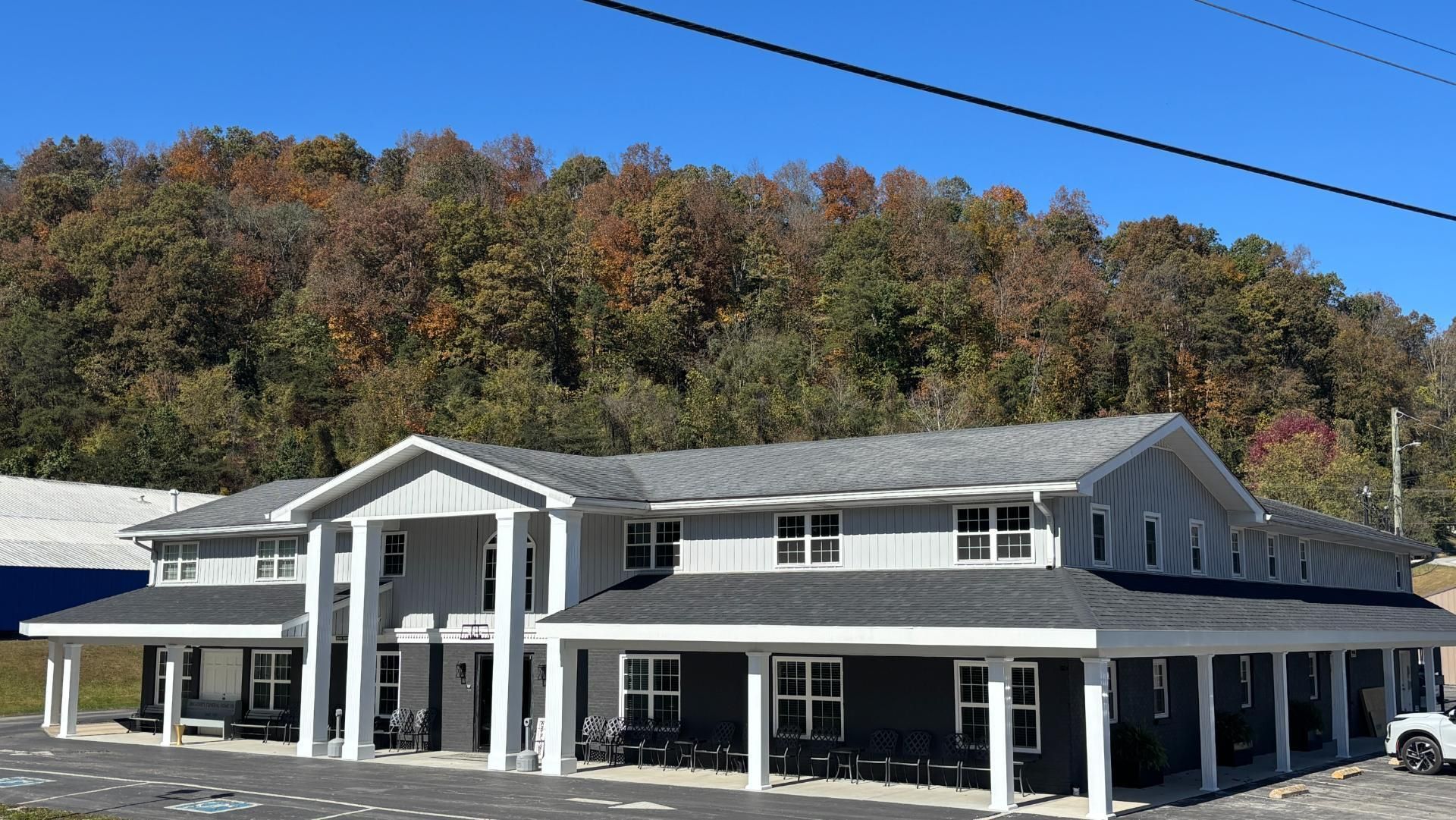 Two-story gray building with white columns and a mountain backdrop under a blue sky