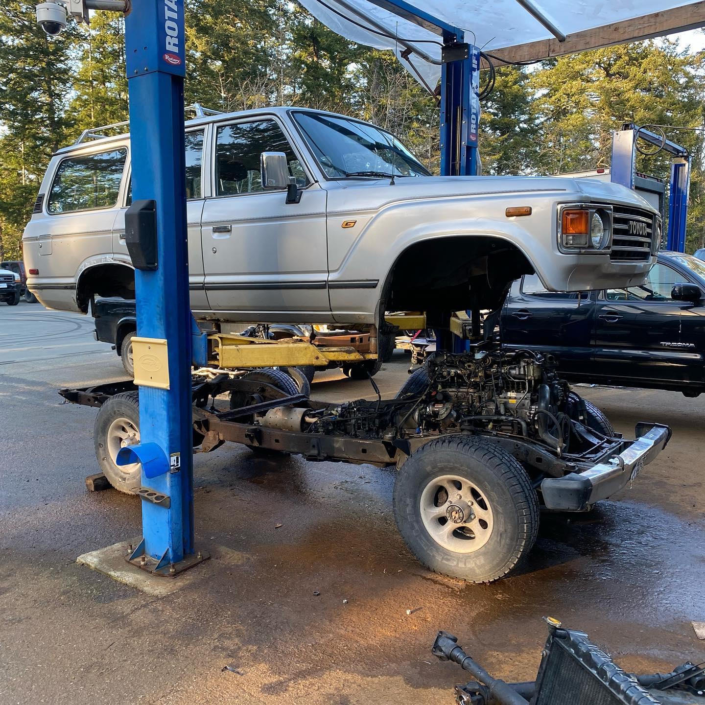 Silver Toyota Land Cruiser on a lift, separated from its chassis at a repair shop.