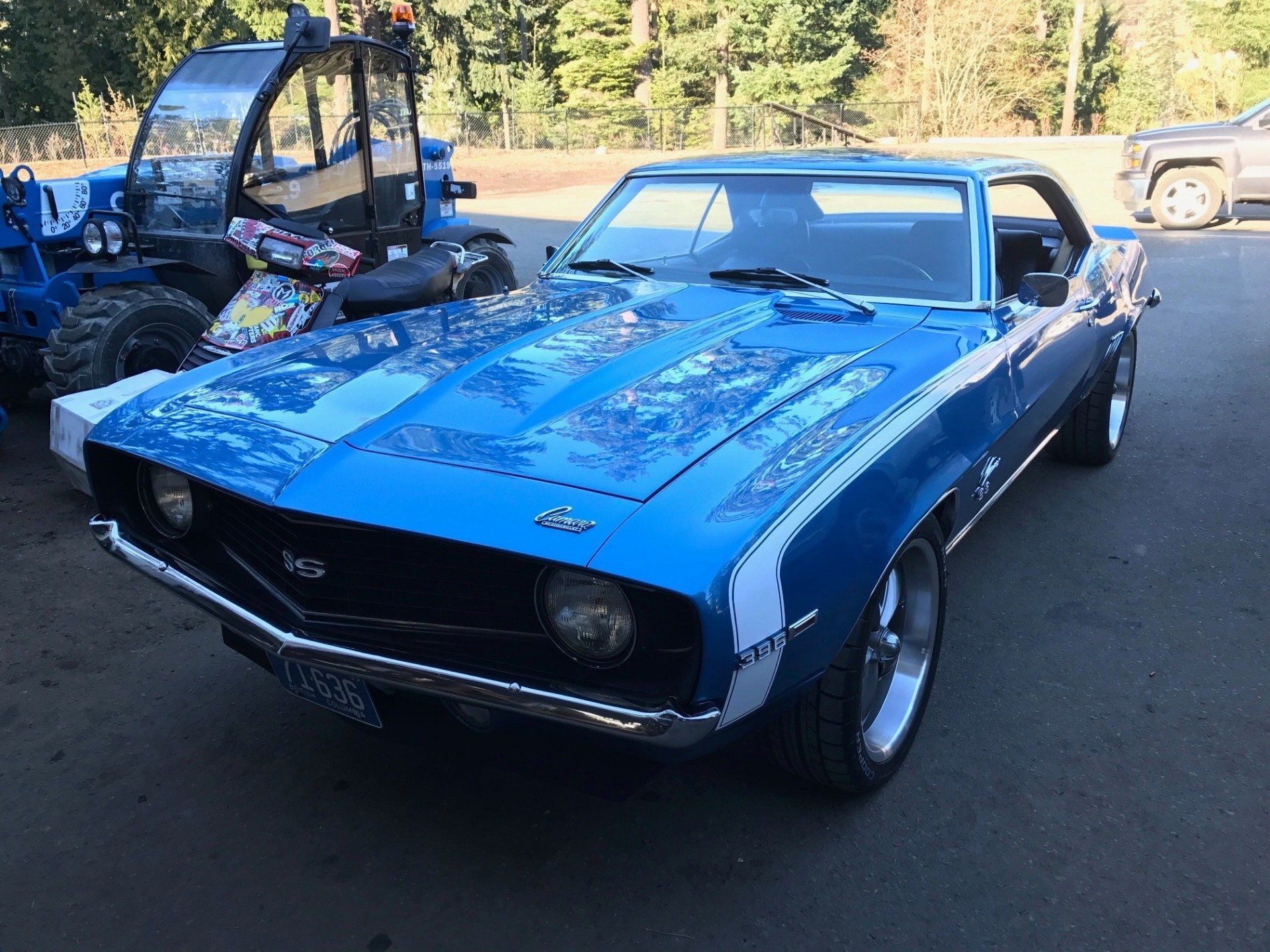 Blue classic 1969 Chevrolet Camaro SS parked in front of a blue tractor.