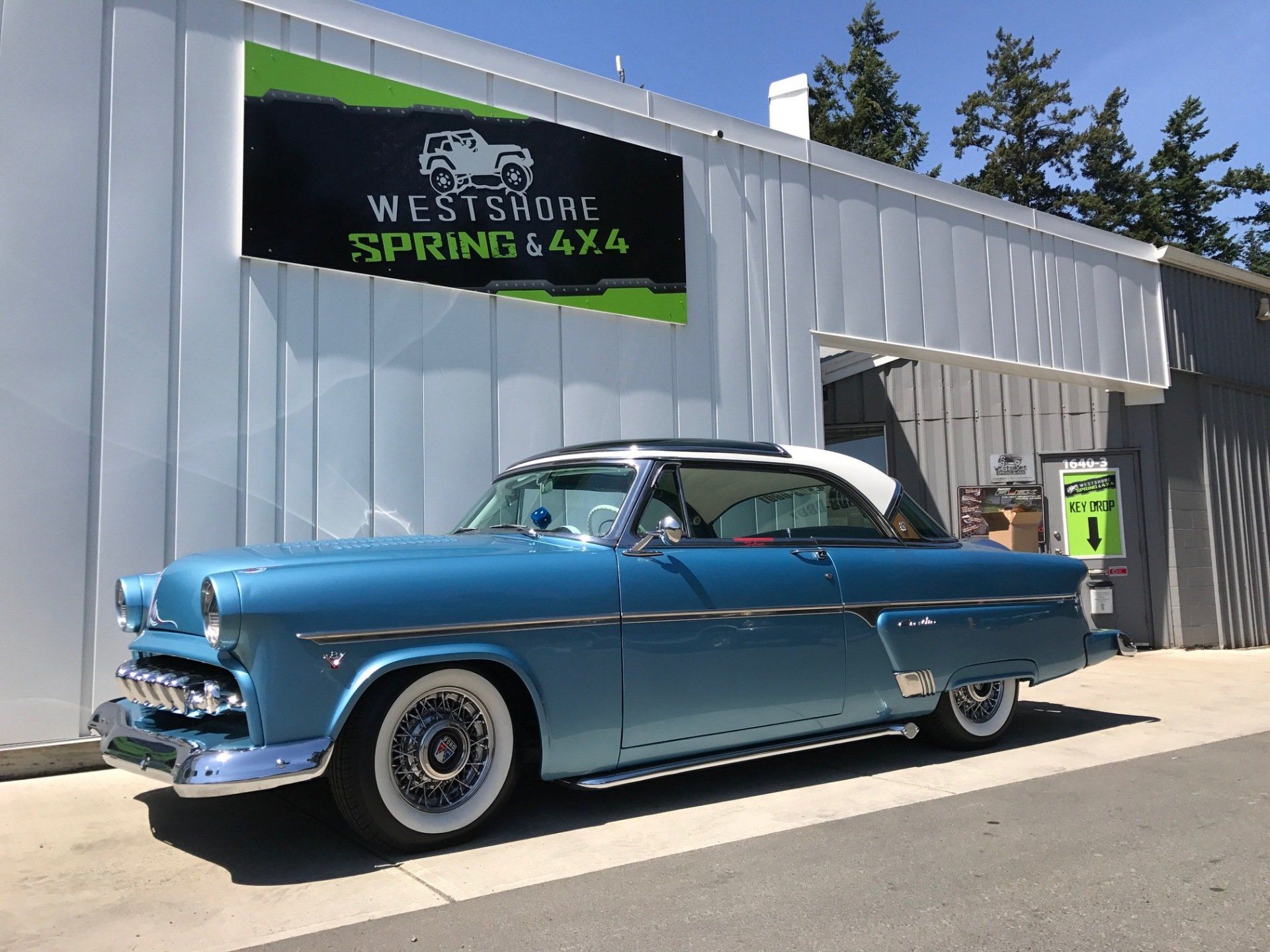 Blue classic car parked outside a shop with a