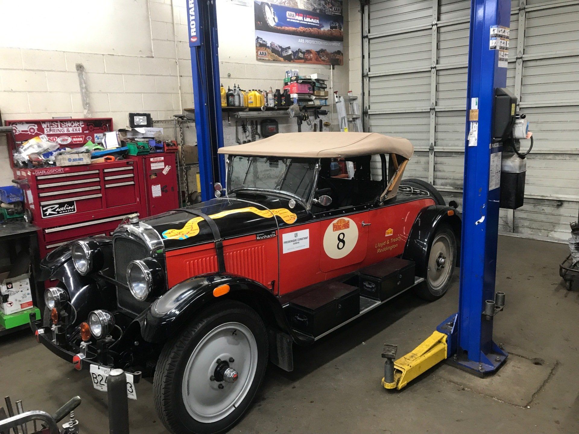 Classic red and black car on a lift in a garage. Beige top, round