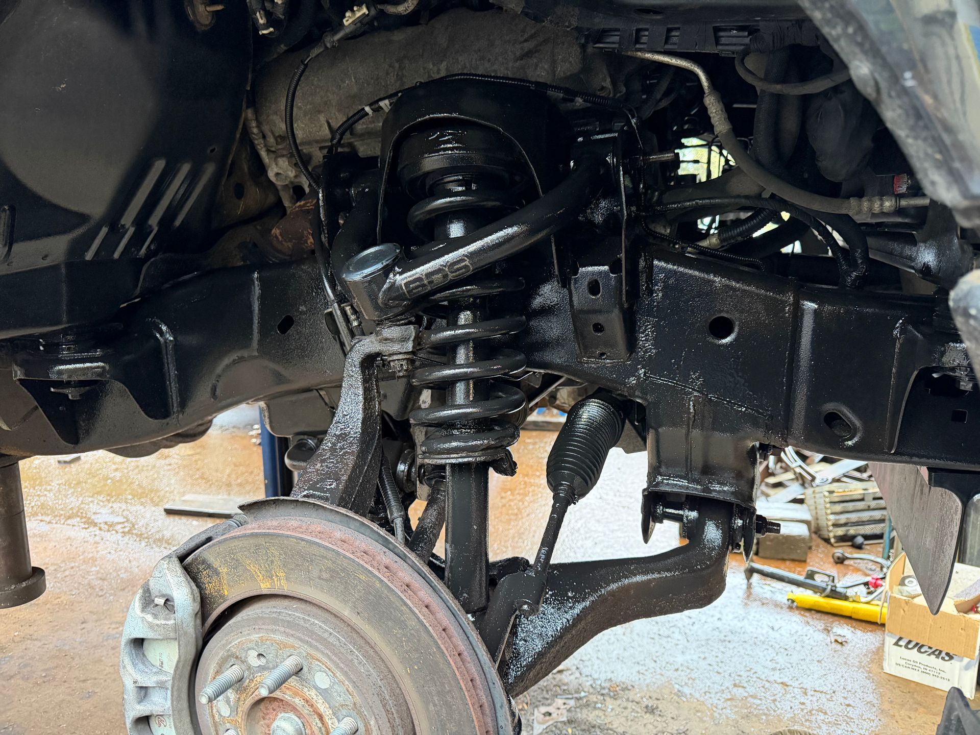 Black painted car suspension components; close-up view; with shock absorber, control arms, and brake rotor visible.