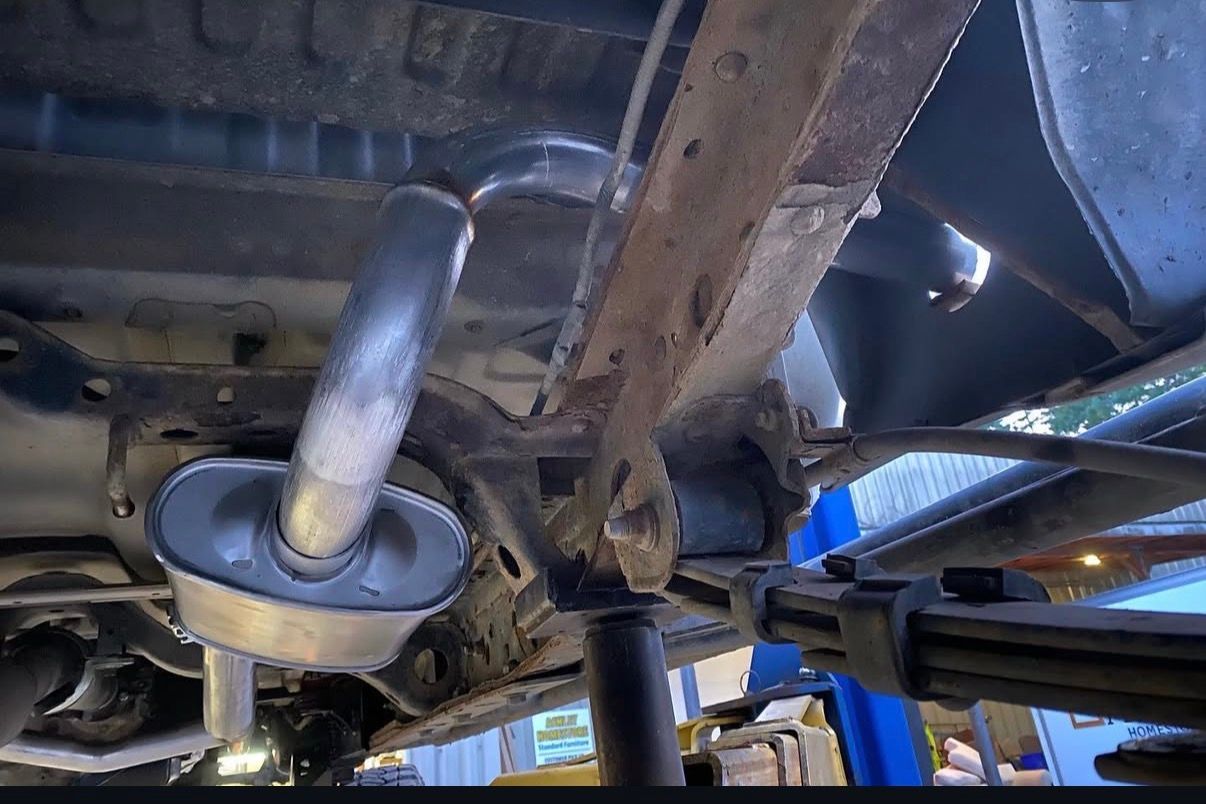 Underside of a vehicle, showing exhaust system, suspension components, and rust.