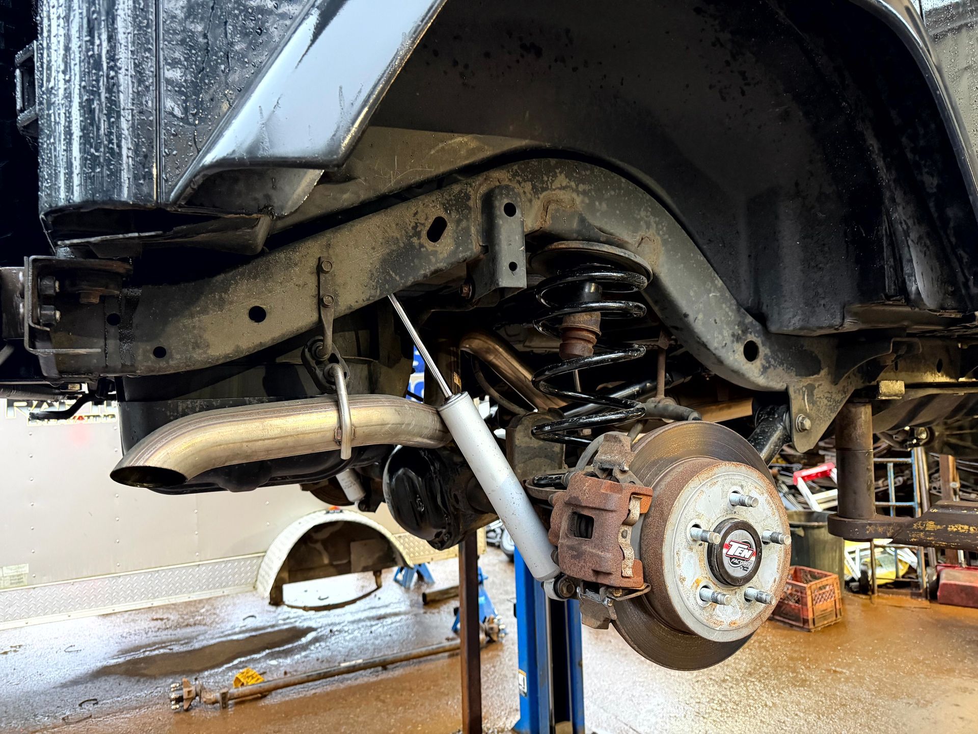 Rear suspension of a black off-road vehicle; spring, shock absorber, brake disc, and exhaust pipe visible.
