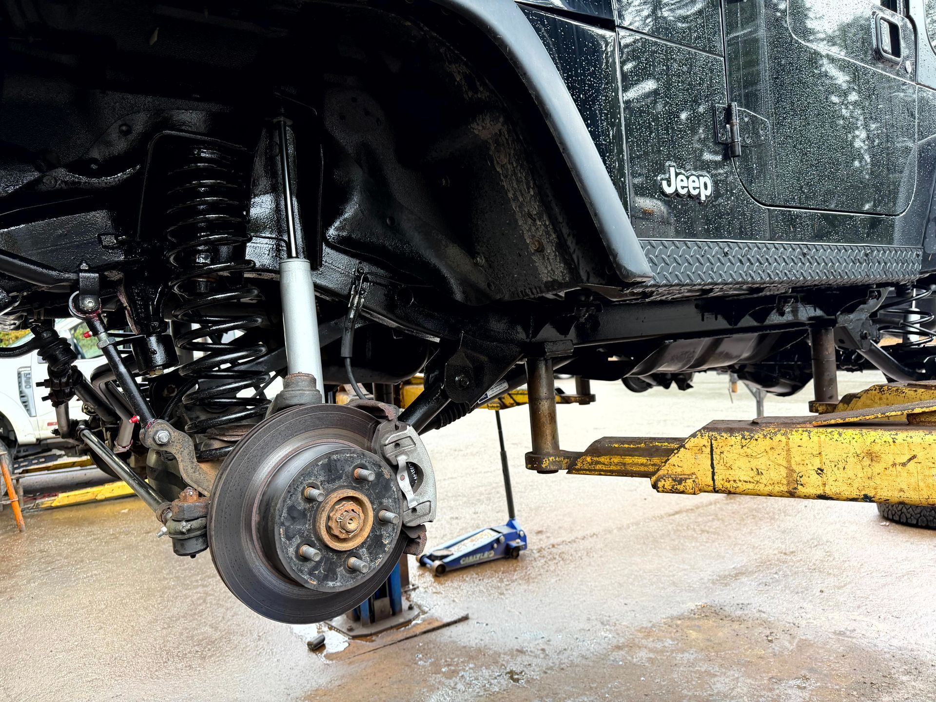 Black Jeep underside raised on a lift, showing suspension and brakes.