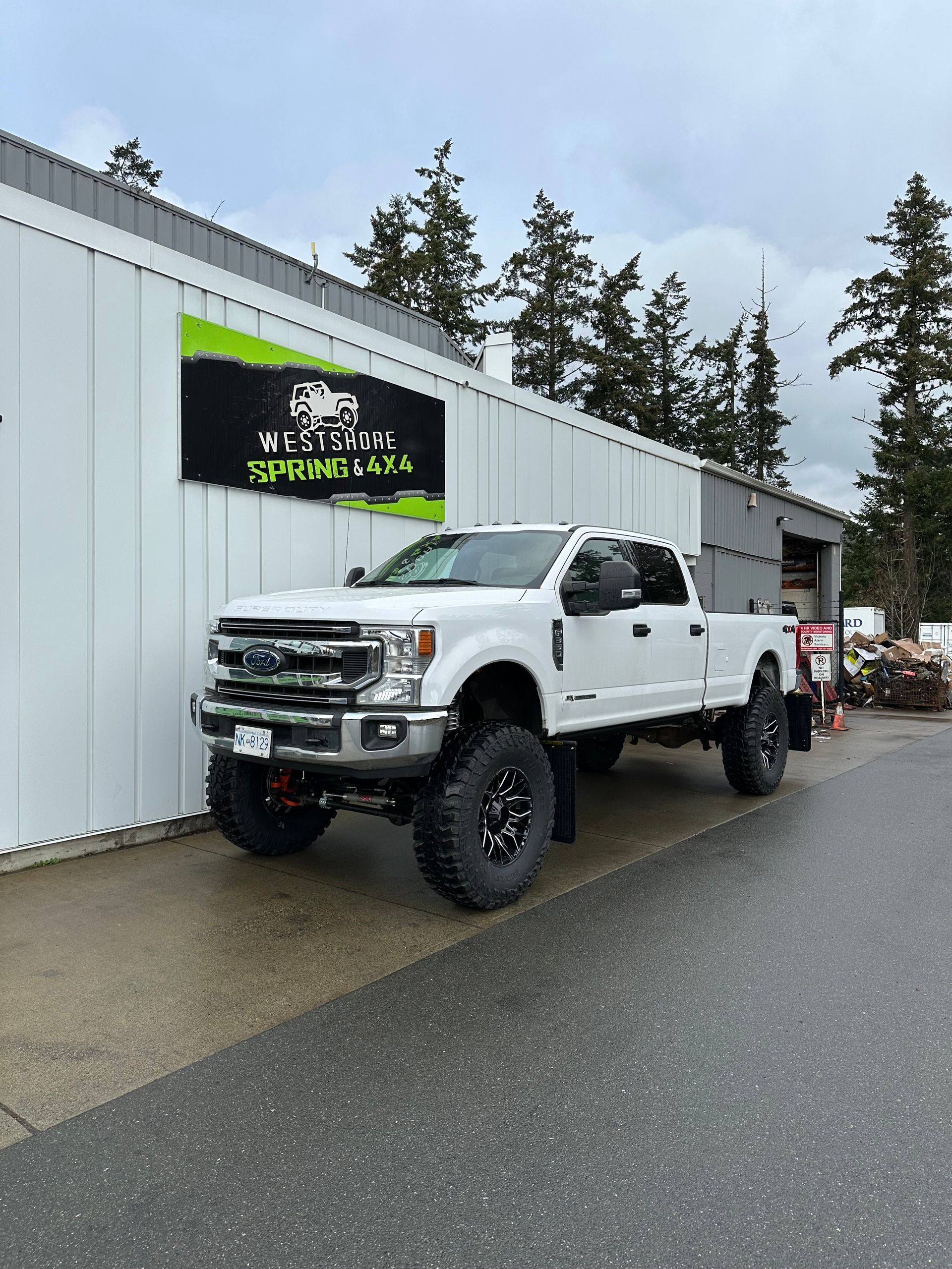 White lifted pickup truck parked in front of a building with a company sign, cloudy day.