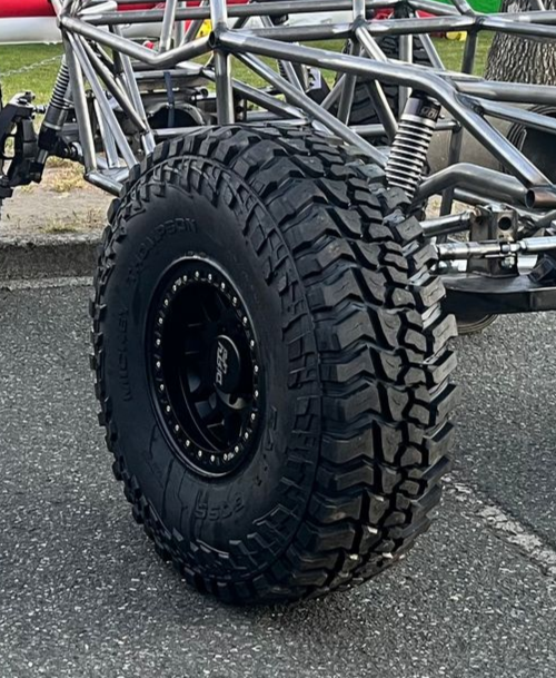 Close-up of a large, black off-road tire and wheel on a vehicle frame, on asphalt.