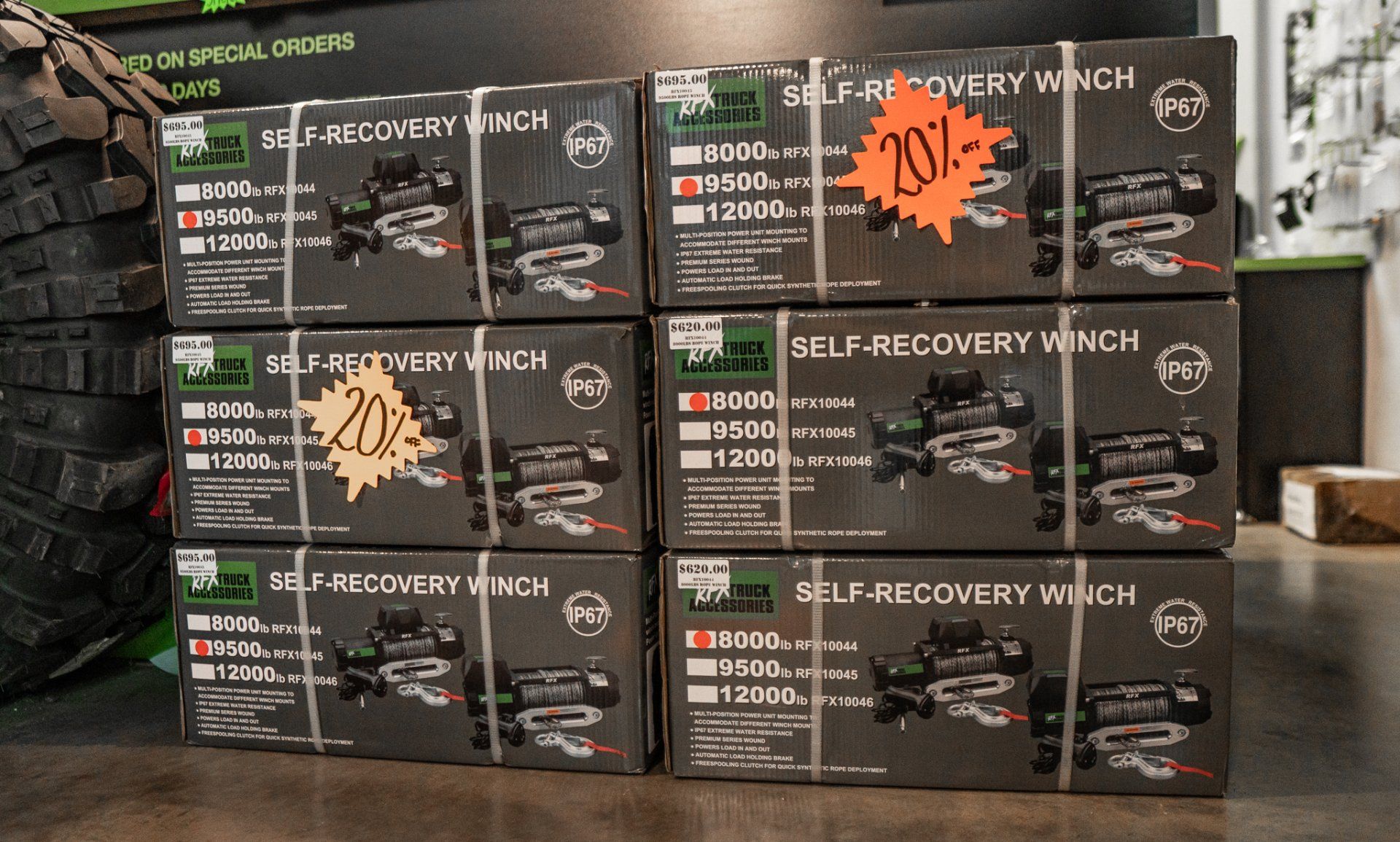 Boxes of self-recovery winches with sale stickers. Dark boxes, green labels, sitting on a wooden surface.